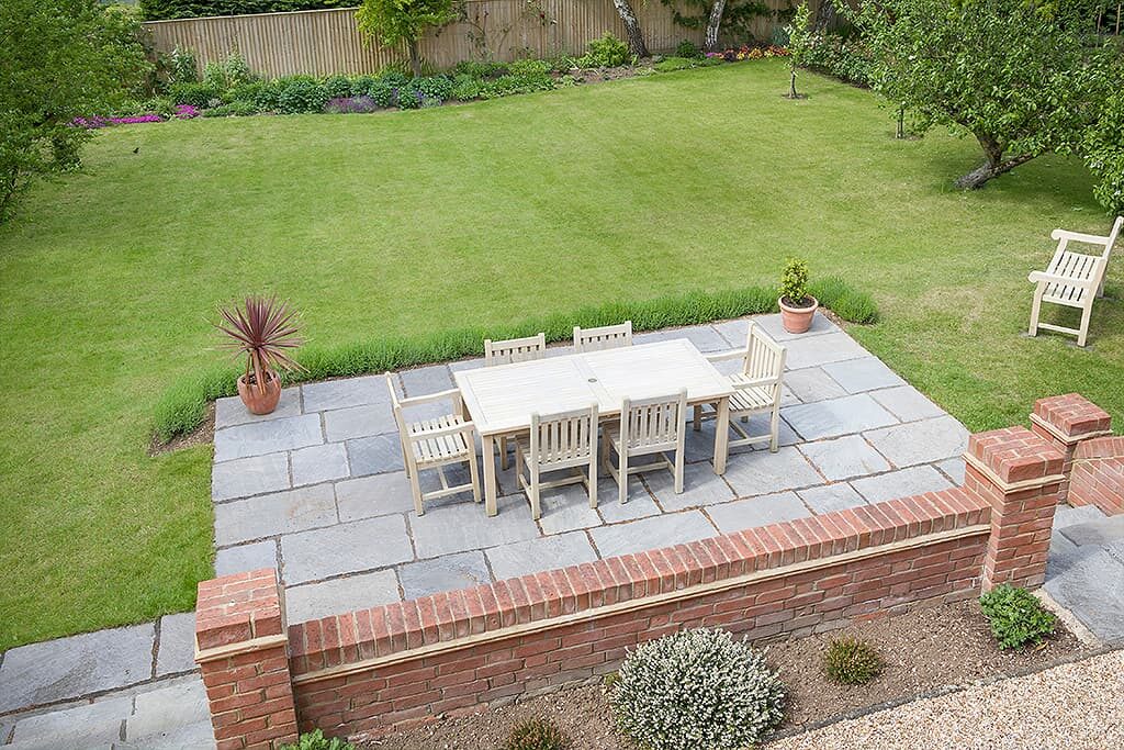 Grey flagstone patio with a low brick wall and garden furniture